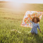 Cute african baby girl at the field on the sunset playing with kite